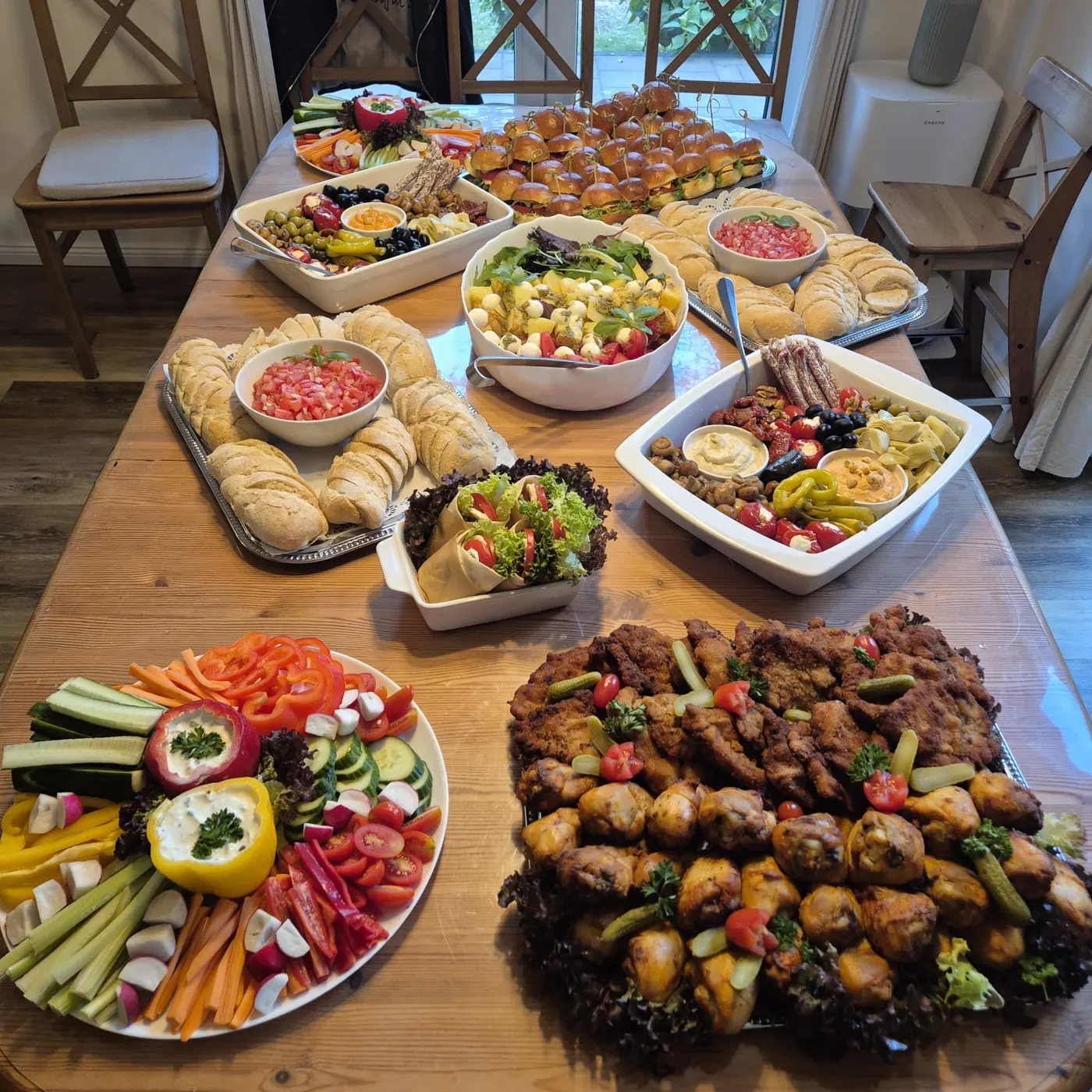 Buffet on a wooden table with a vegetable platter, meatballs, salads and rolls