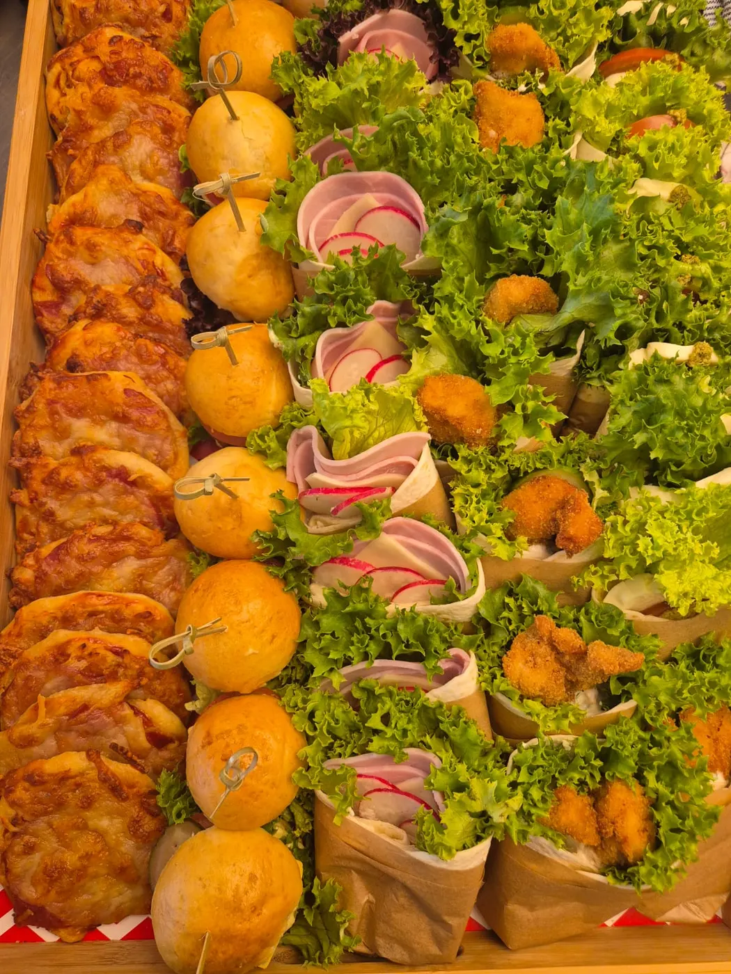 Platter with mini rolls, pizza swirls and wraps on a bed of salad