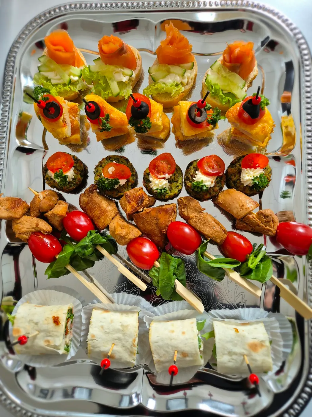Finger food on a silver tray with salmon, stuffed mushrooms, skewers and wraps