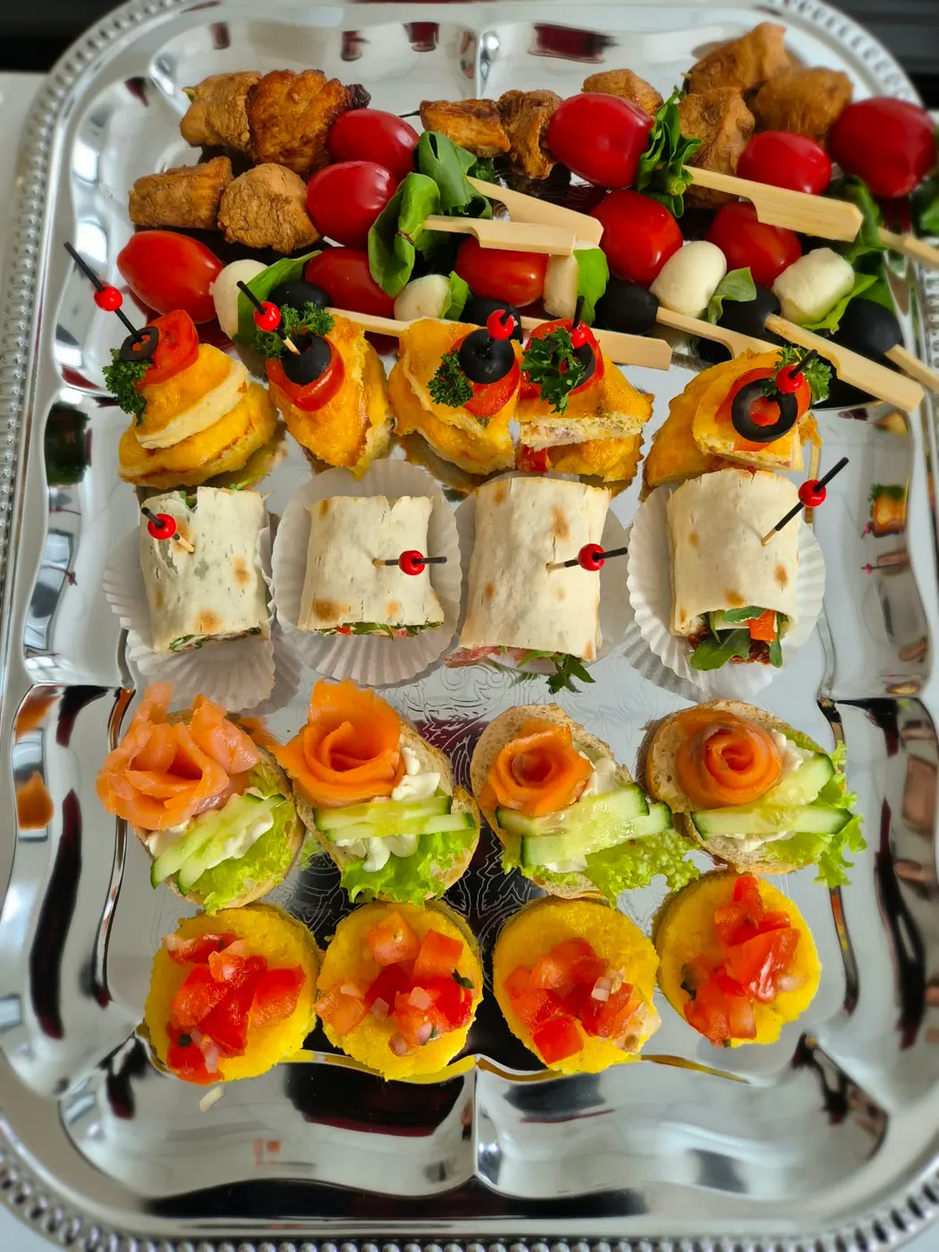 Finger food on a silver tray with wraps, salmon rolls and skewers
