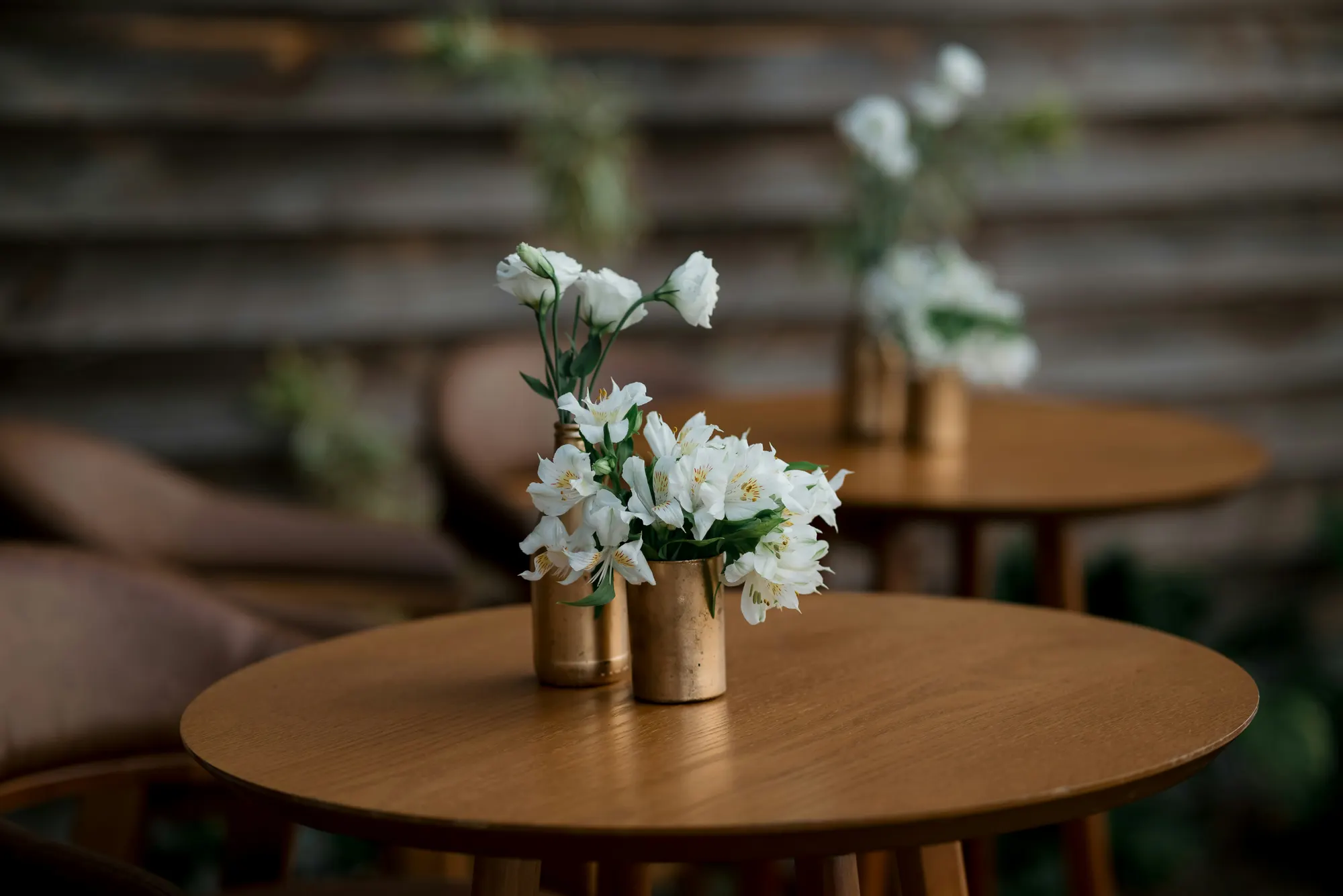 Runde Holztische mit weißen Blumen in schlichten Vasen