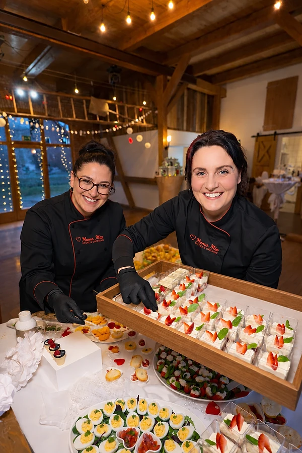 Two Mama Mia cooks in black chef jackets smiling behind a tray of strawberry desserts